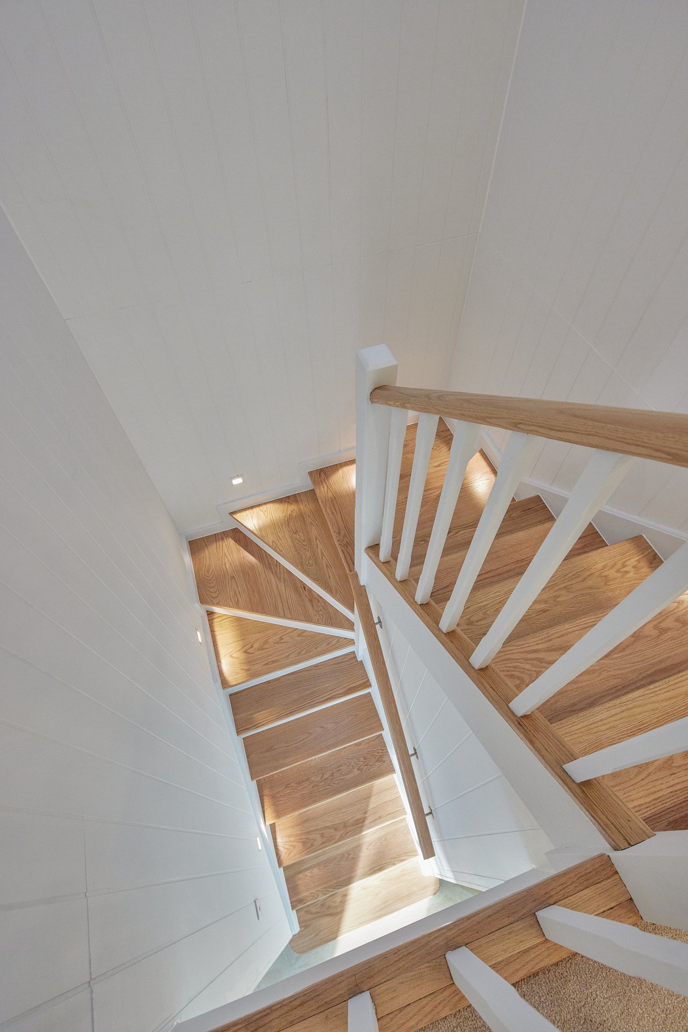 View of a wooden staircase with white railings and walls, illuminated by small built-in wall lights.