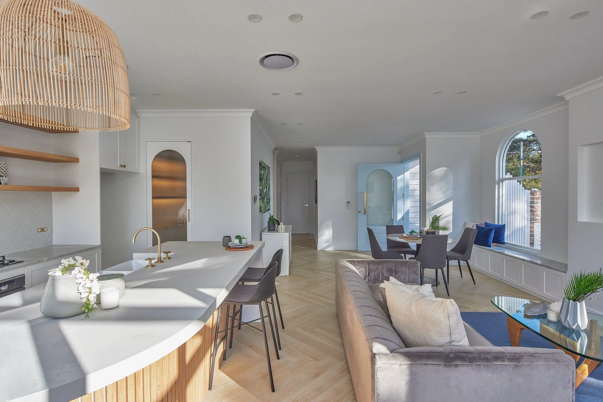 Open-concept living room and kitchen with light-colored furniture, large windows, and natural light.