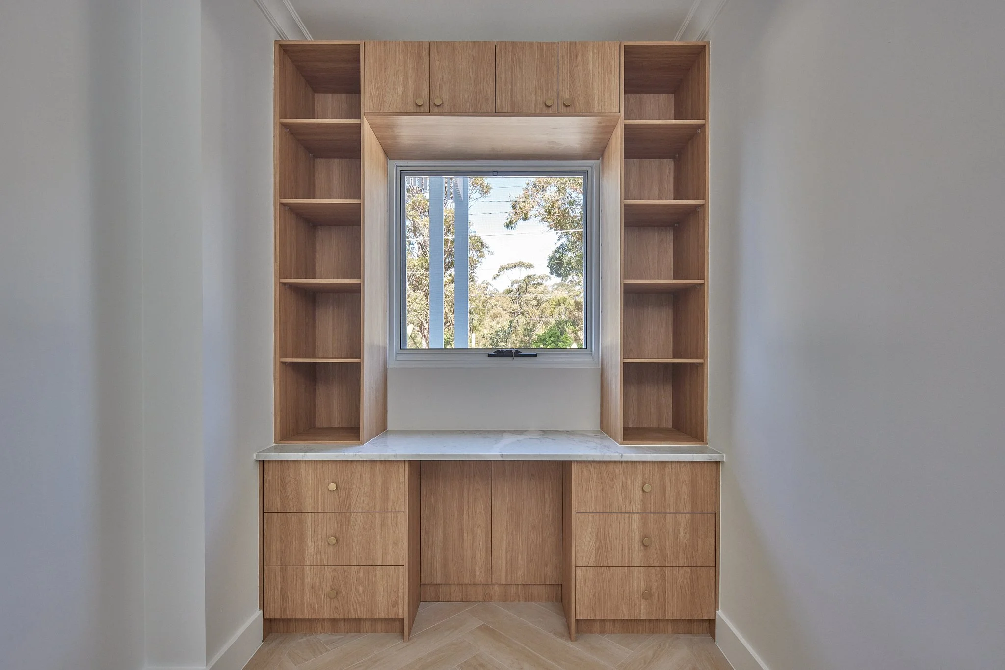 Wooden cabinetry with open shelves on sides, a window in the center, and drawers below, in a minimalistic room.