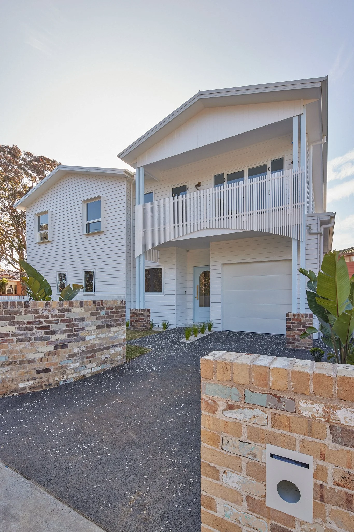 Modern two-story white house with balcony, brick and concrete driveway, and brick mailbox in front.