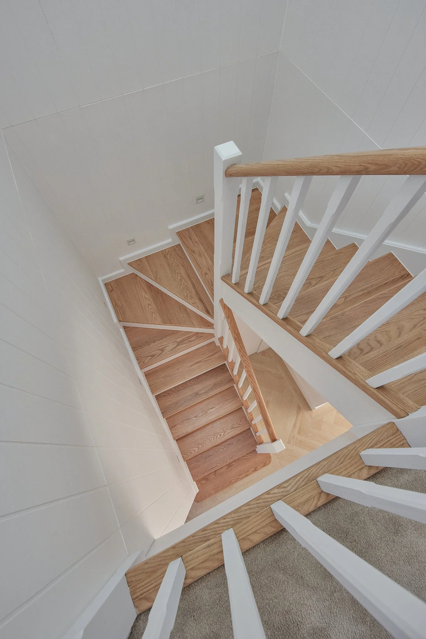 A top-down view of a wooden staircase with white railings and a beige carpeted landing.