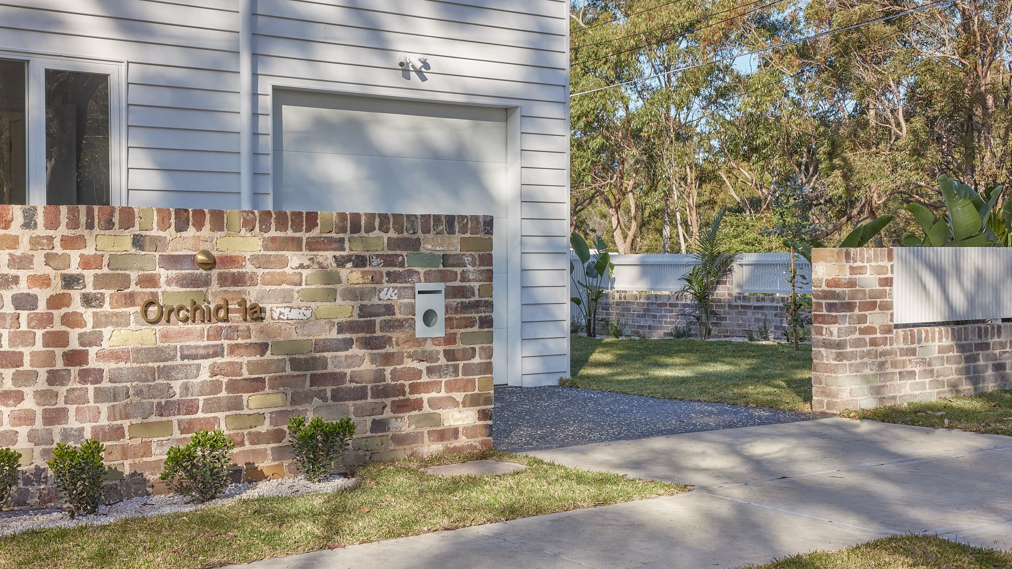 Exterior view of a house with a brick wall, a white metal fence, and a mailbox.