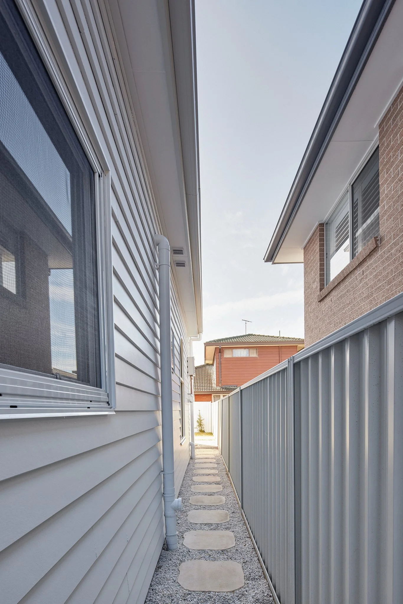 Narrow outdoor pathway between two houses with a stepping stone path, white on one side and brick on the other.
