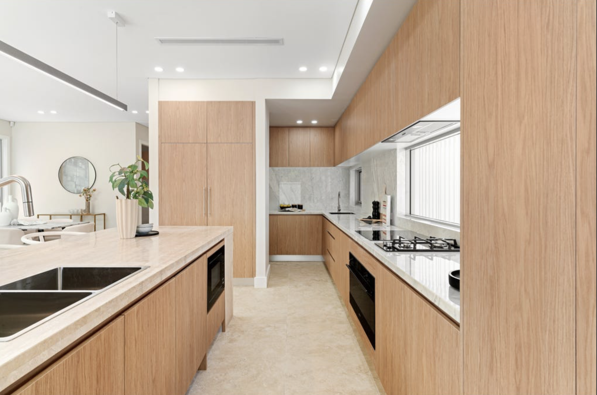 Modern kitchen with wooden cabinets, white marble countertops, stainless steel sink, gas stove, and natural light from a large window.