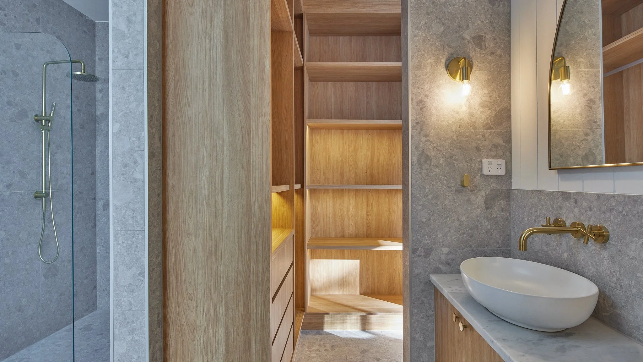Modern bathroom with a shower area, wooden shelves, a vanity with a vessel sink, and brass fixtures.