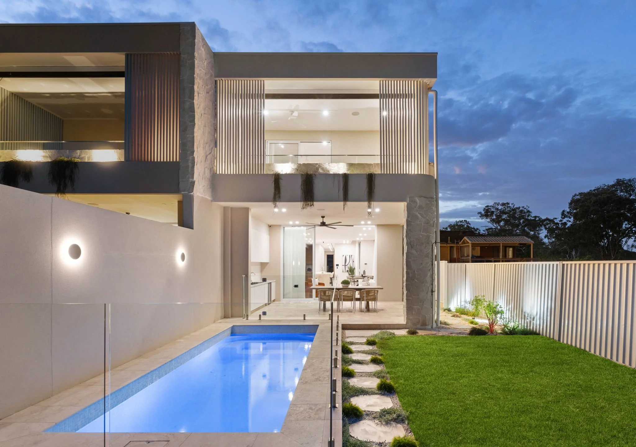 Modern two-story house nighttime exterior view with illuminated interior, outdoor pool, and landscaped yard.