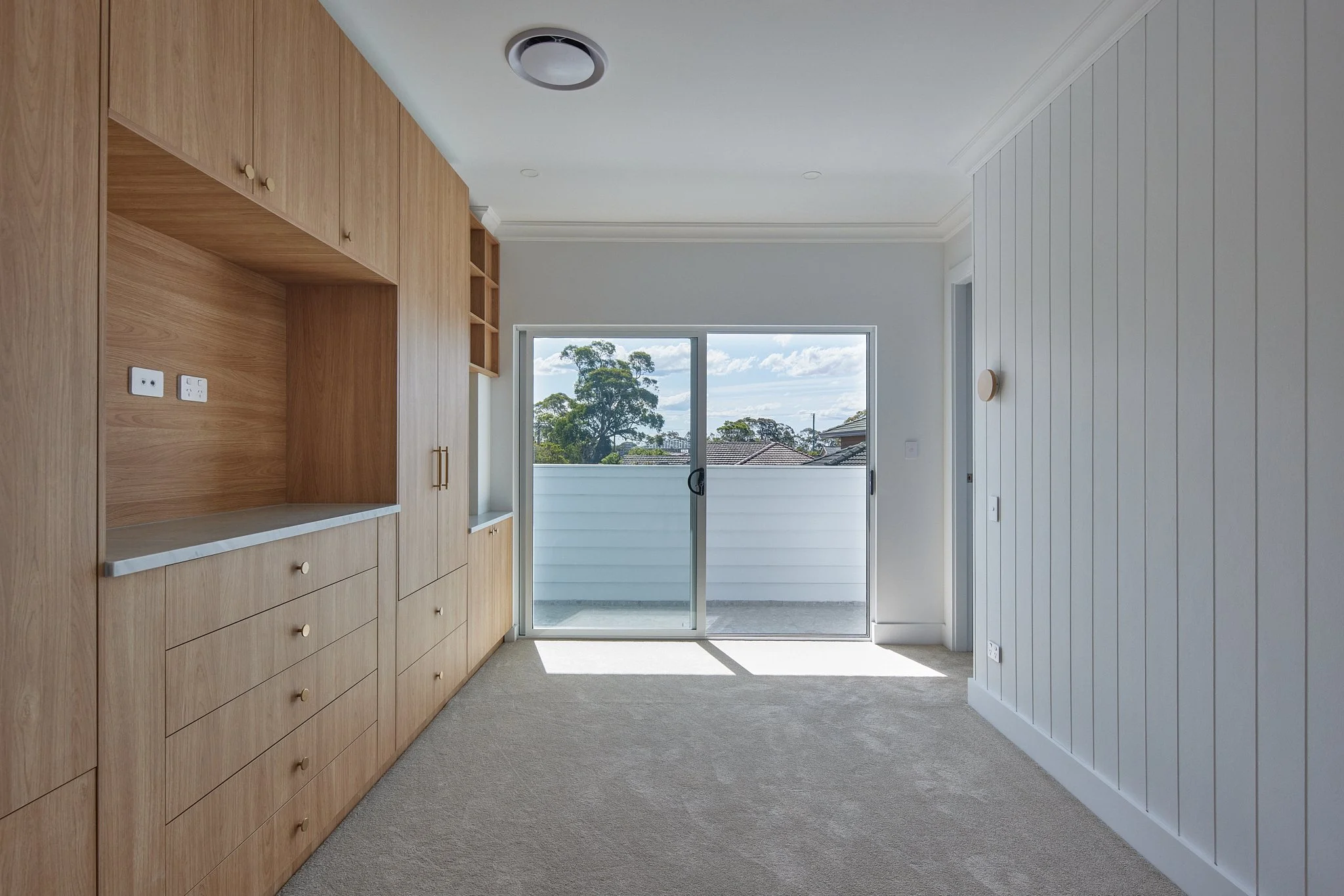 Empty room with built-in wooden cabinets, sliding glass door leading to balcony, white walls, and beige carpet