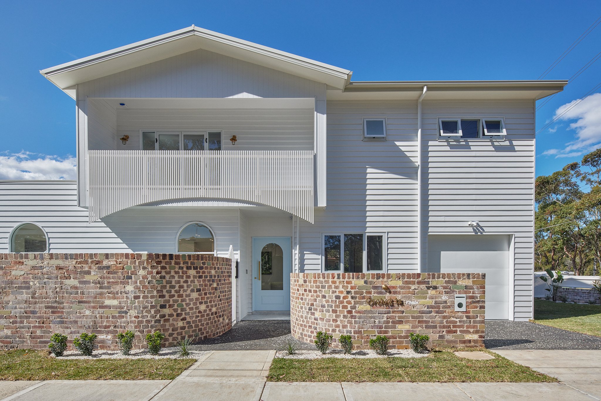 Modern two-story house with white siding, a brick wall front, and small garden, under a clear blue sky.