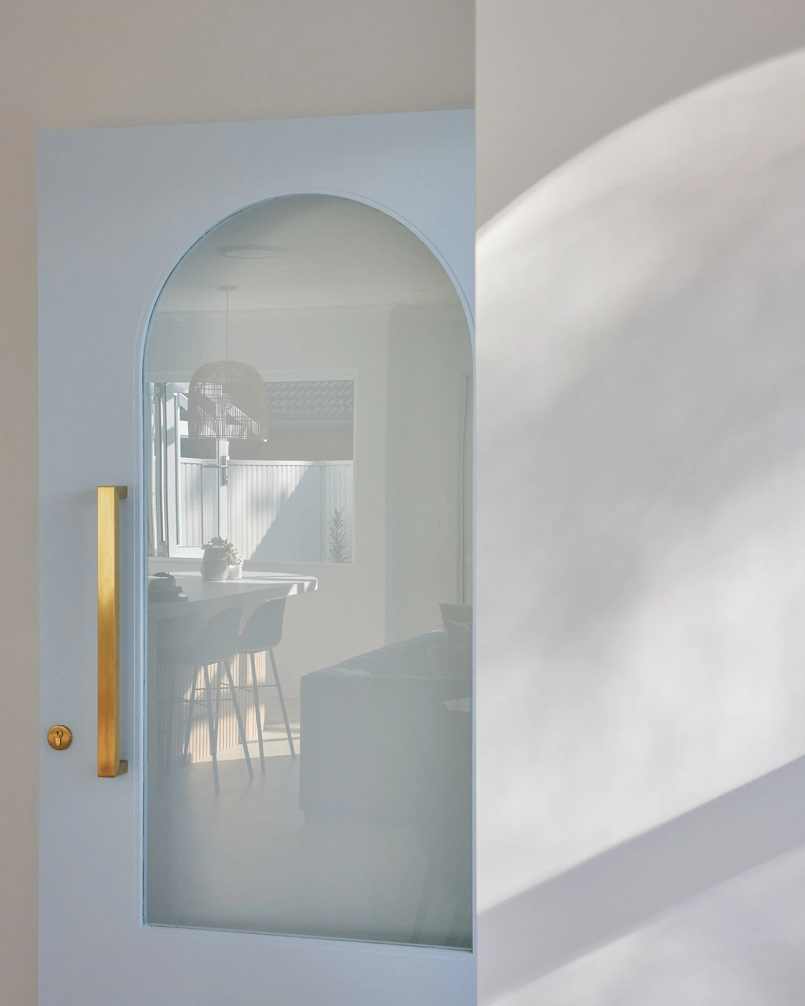 View through a frosted glass door into a dining area with a table, chairs, window, and hanging light fixture in a bright, modern interior.