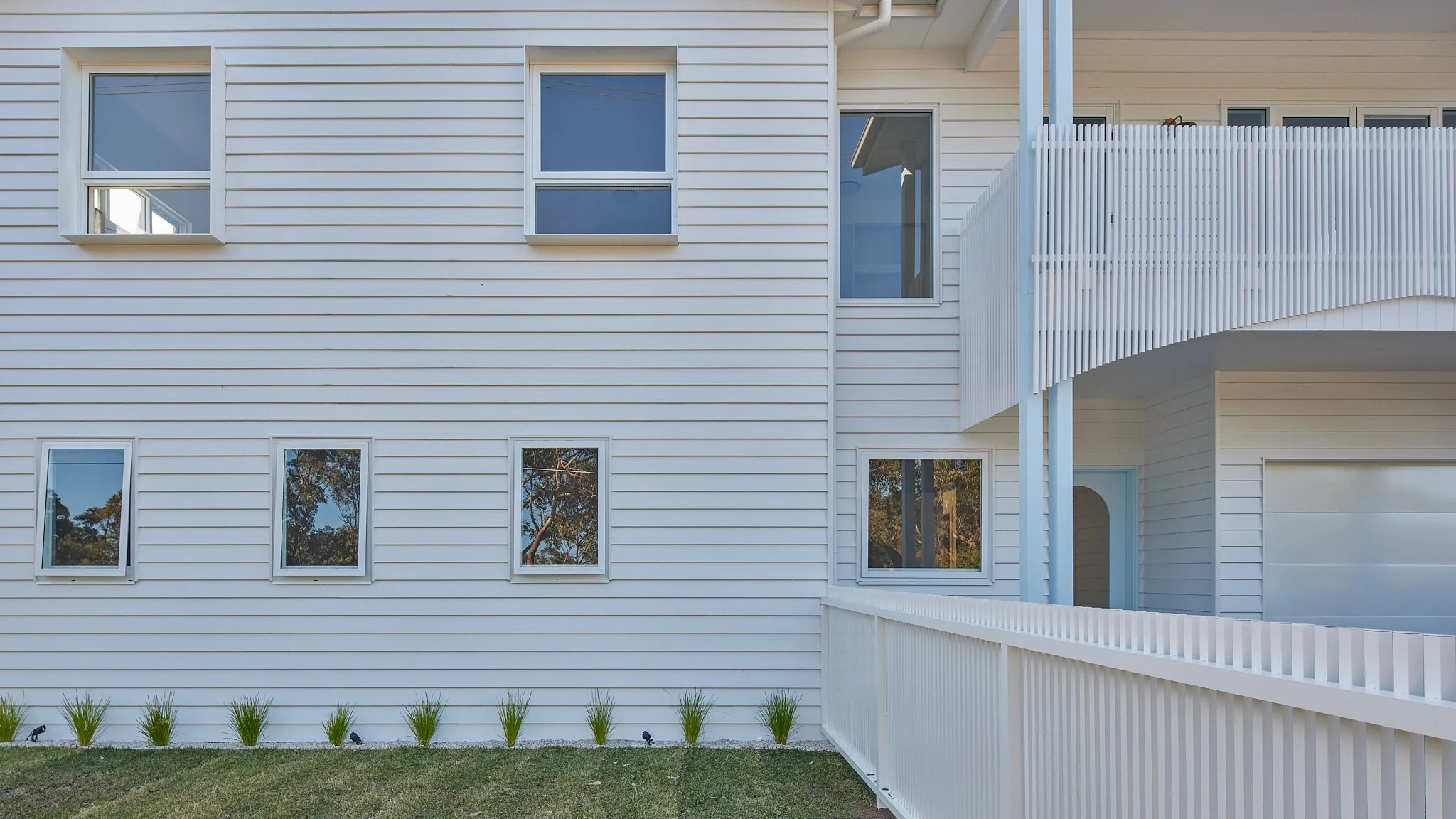 Exterior view of a white multi-story house with horizontal siding, several windows, and a white fence.