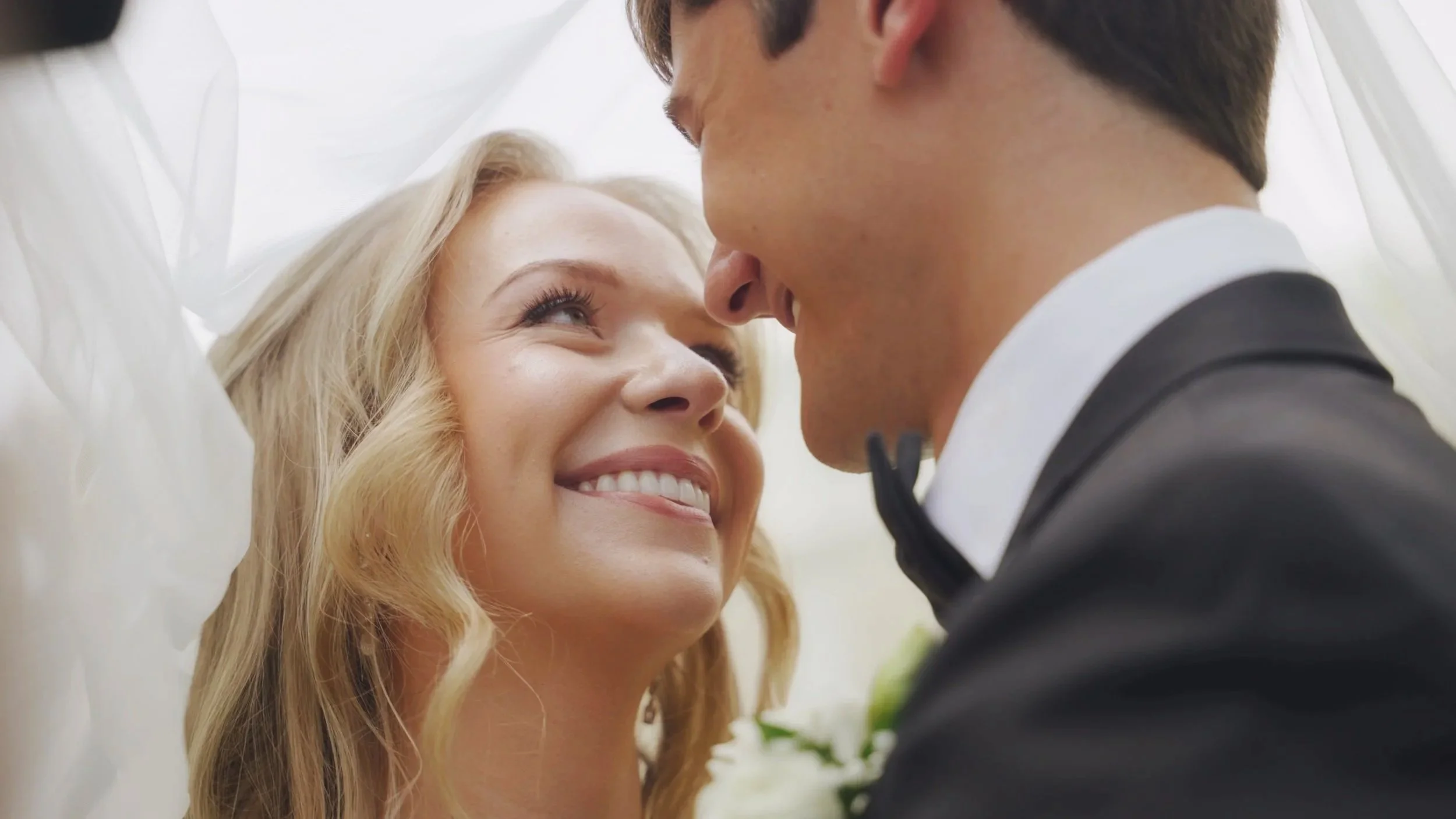 A bride and groom smiling at each other close-up at their wedding, with the bride looking up at the groom.