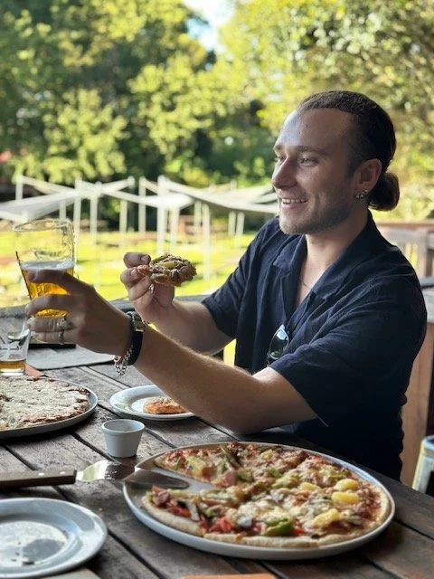 Man enjoying pizza and beer outdoors at a picnic table.
