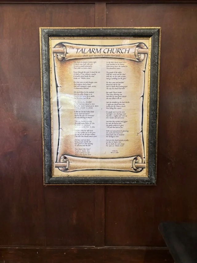 A framed poem titled "The Talam Church" on a dark wooden wall.