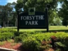 Sign that reads 'Forsythe Park' surrounded by green bushes and trees in the background.