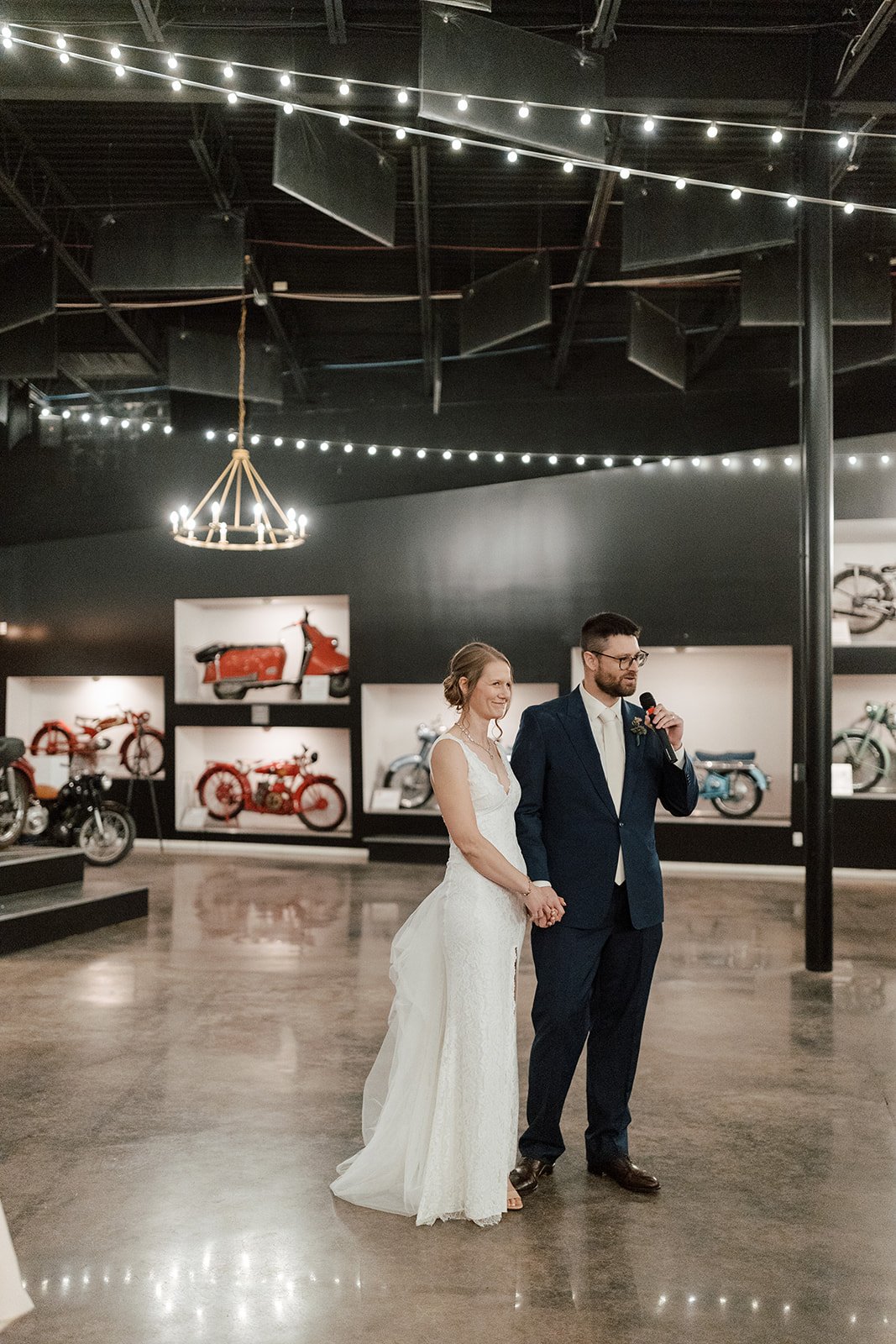 smith and company interior event space at the moto museum event venue st. louis showing vintage motorcycles in the background attached to wall and a bride and groom giving a welcome speech at wedding