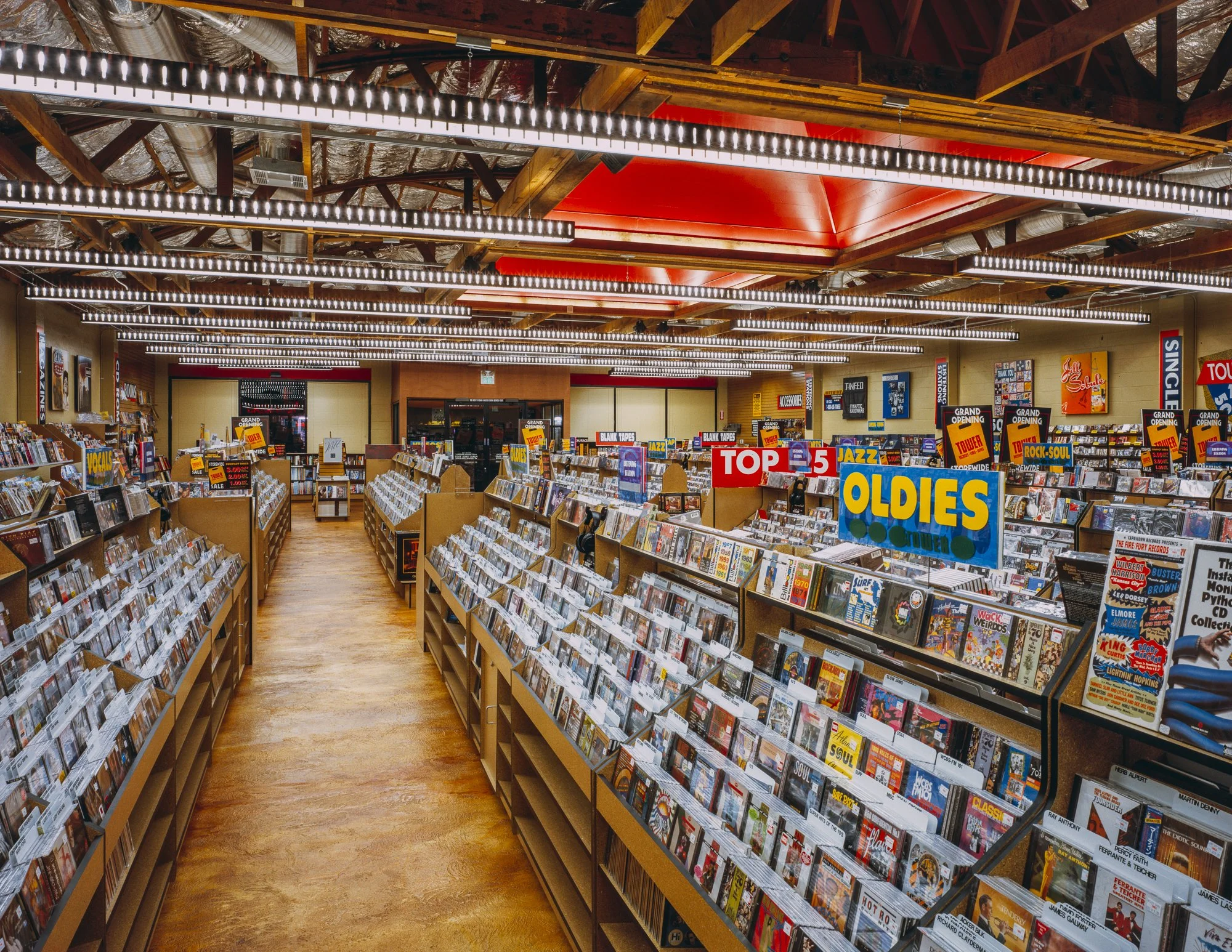 The finishes form the backdrop to the store’s cultural heart, rows and rows of CD, book, and magazine racks that fully occupy the existing rectangular plan. New oriented strand board (OSB) racks celebrate Tower Record’s access to the zeitgeist throug