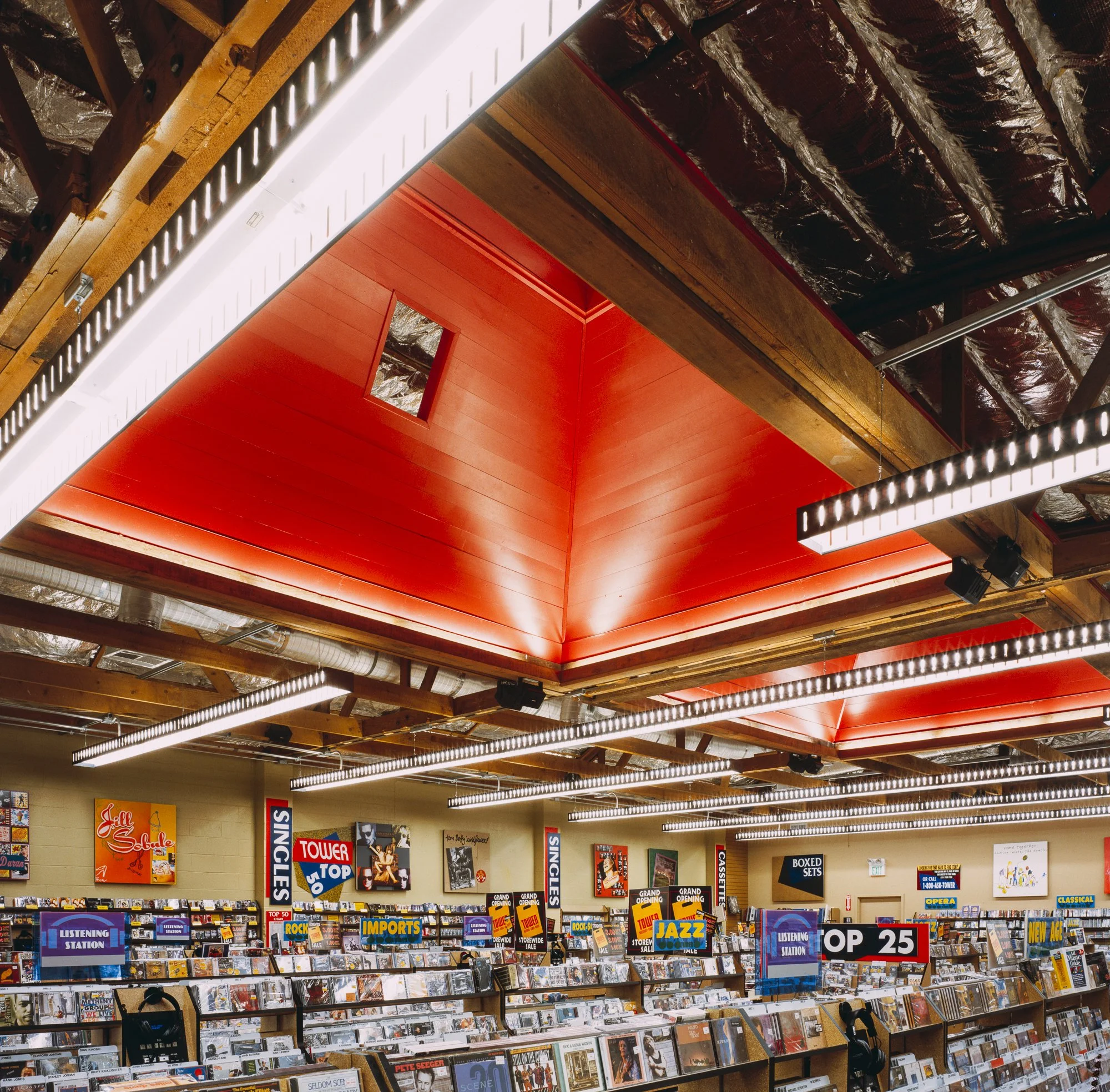I exposed the ceiling and skylight structures inside the space by removing the existing T-bar ceiling, dramatically adding height and light. Intricate rows of industrial lighting show off the supporting beams and red-painted recesses. The existing fl