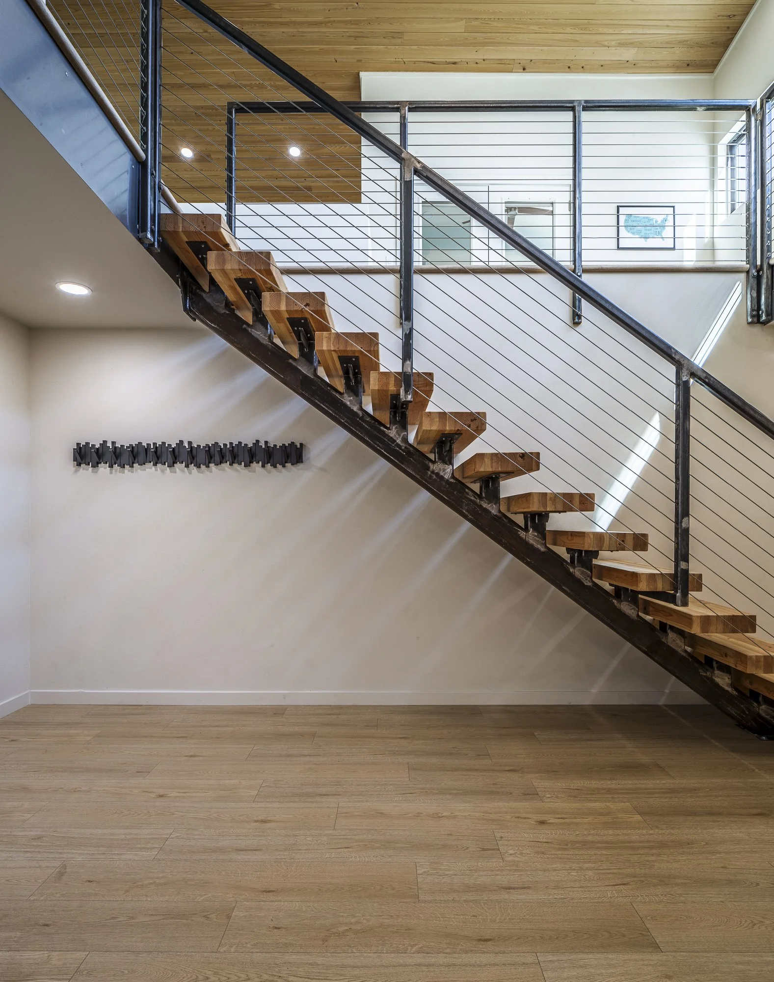 The entry’s custom steel staircase features substantial solid wood plank treads with open risers, complemented by open steel and wire railings.