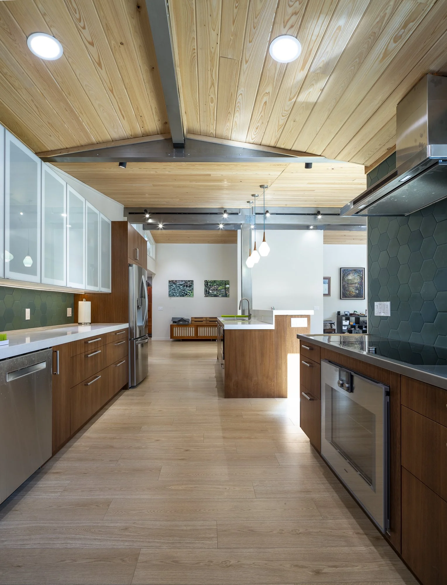 Exposed ceiling beams serve as structural elements and mounting points for track lighting. Galvanized steel trusses mark a change in the roofline over the kitchen area.