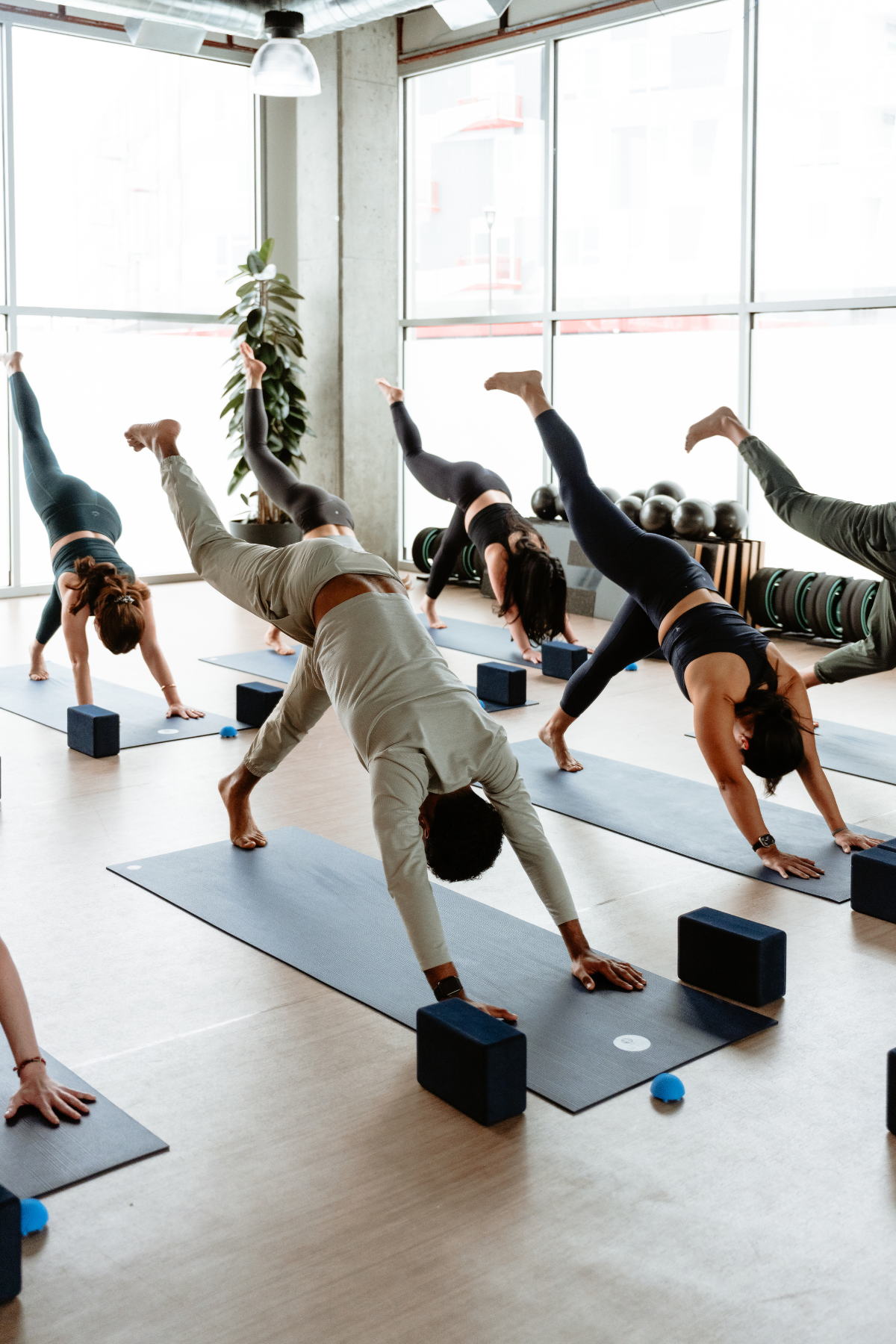 Group of people practicing yoga in a studio, performing downward dog pose on mats with blocks, in a neighborhood wellness club in Denver.