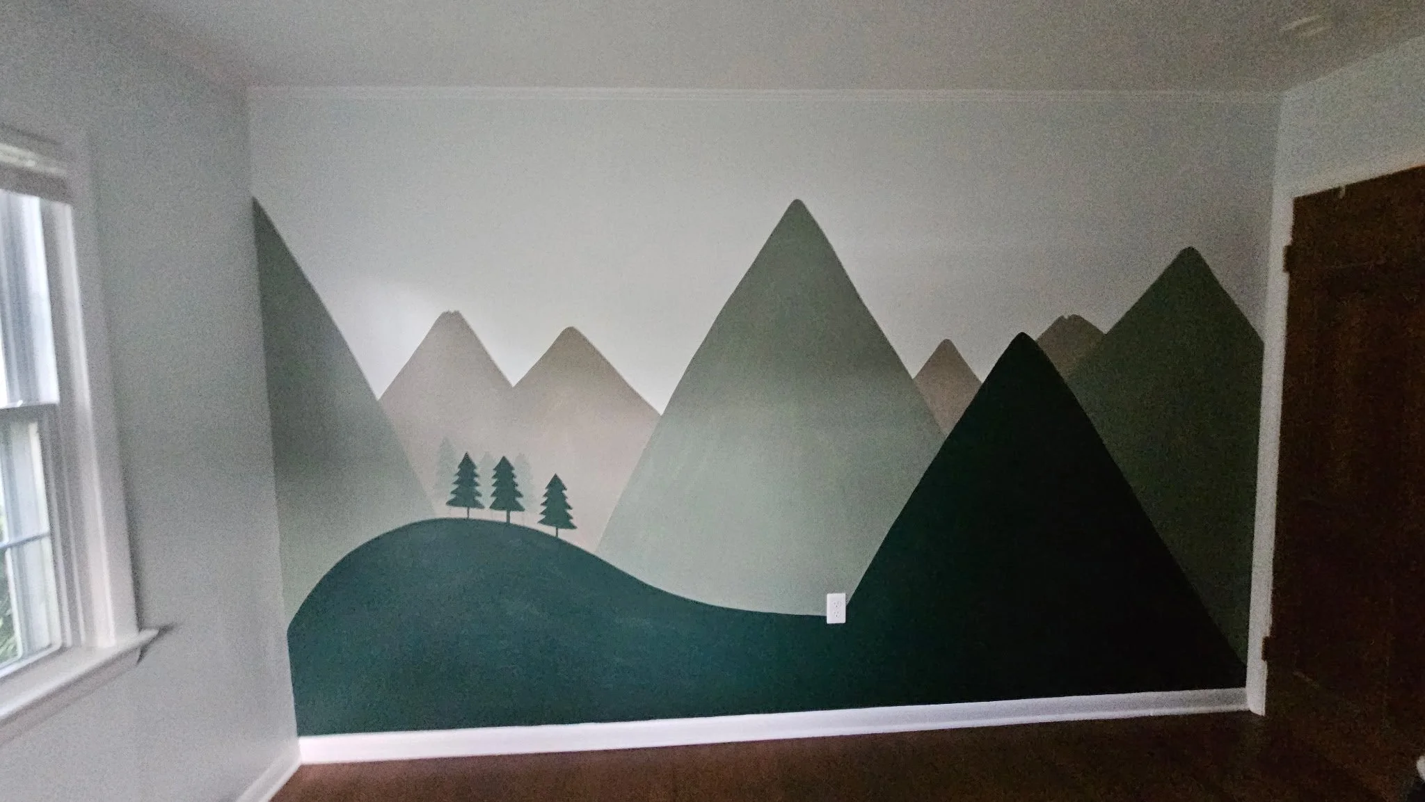 After photo of a freshly painted mural of green mountains in a nursery