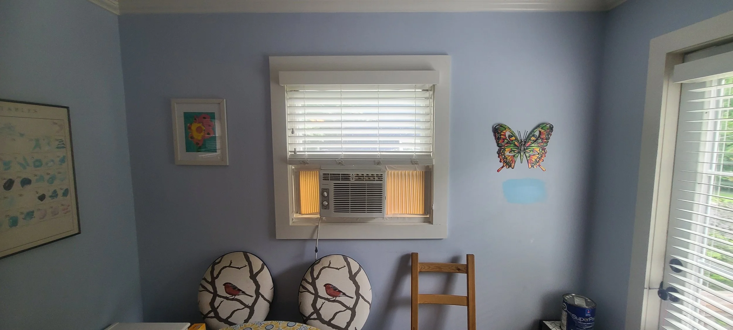 Before photo of a light blue room with a butteryfly on the wall and a window air conditioner