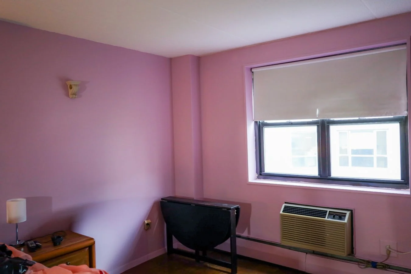 Bedroom with pink walls, a small safe, and a window slightly open