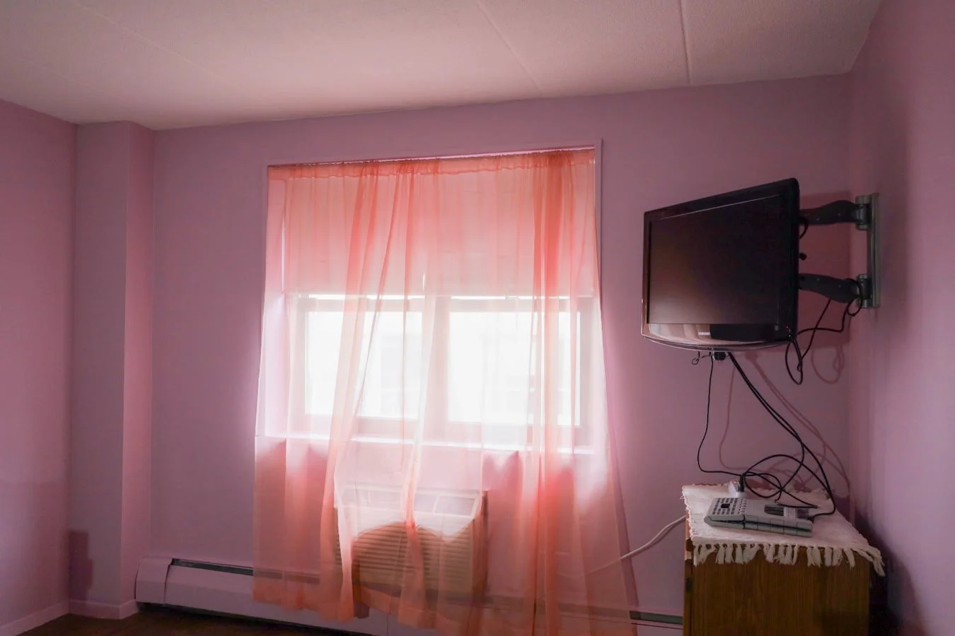 Pink walls with a window, draped with red curtains next to a wall mounted television