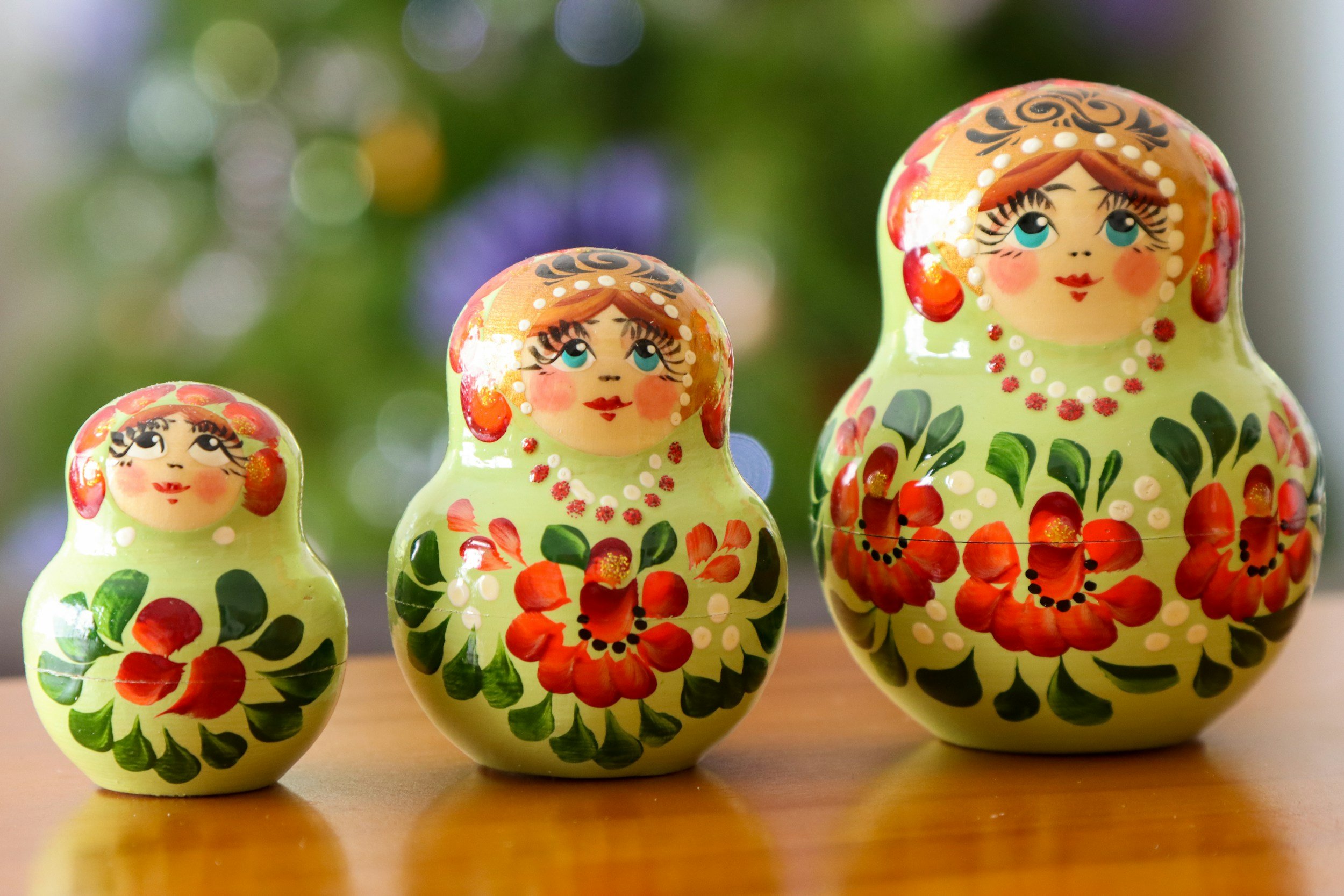 Three brightly colored Russian nesting dolls on a wooden surface with a blurred green background.