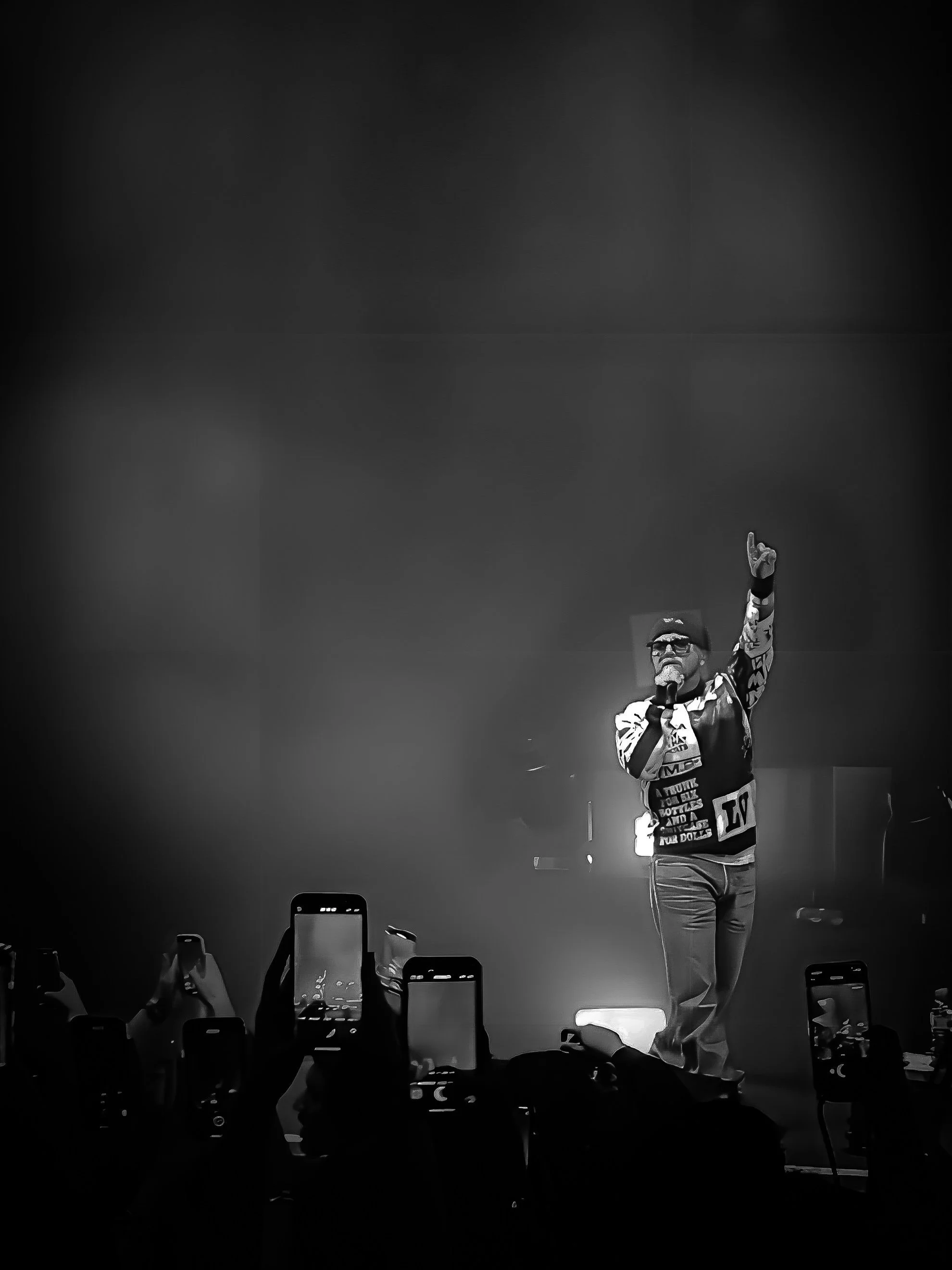 Un artiste sur scène chantant devant une foule tenant des smartphones, capturant le moment en noir et blanc.