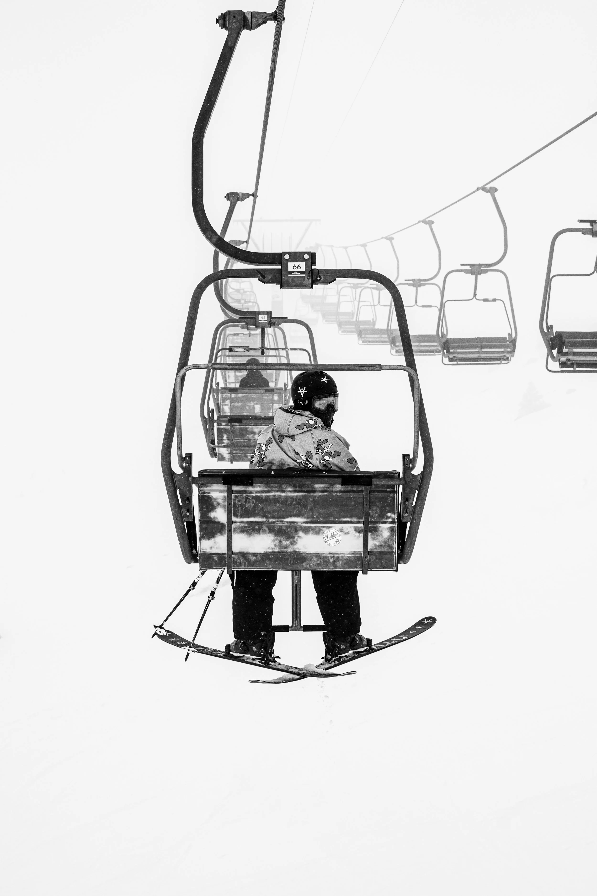 Skieur suspendu sur un télésiège enneigé en noir et blanc.