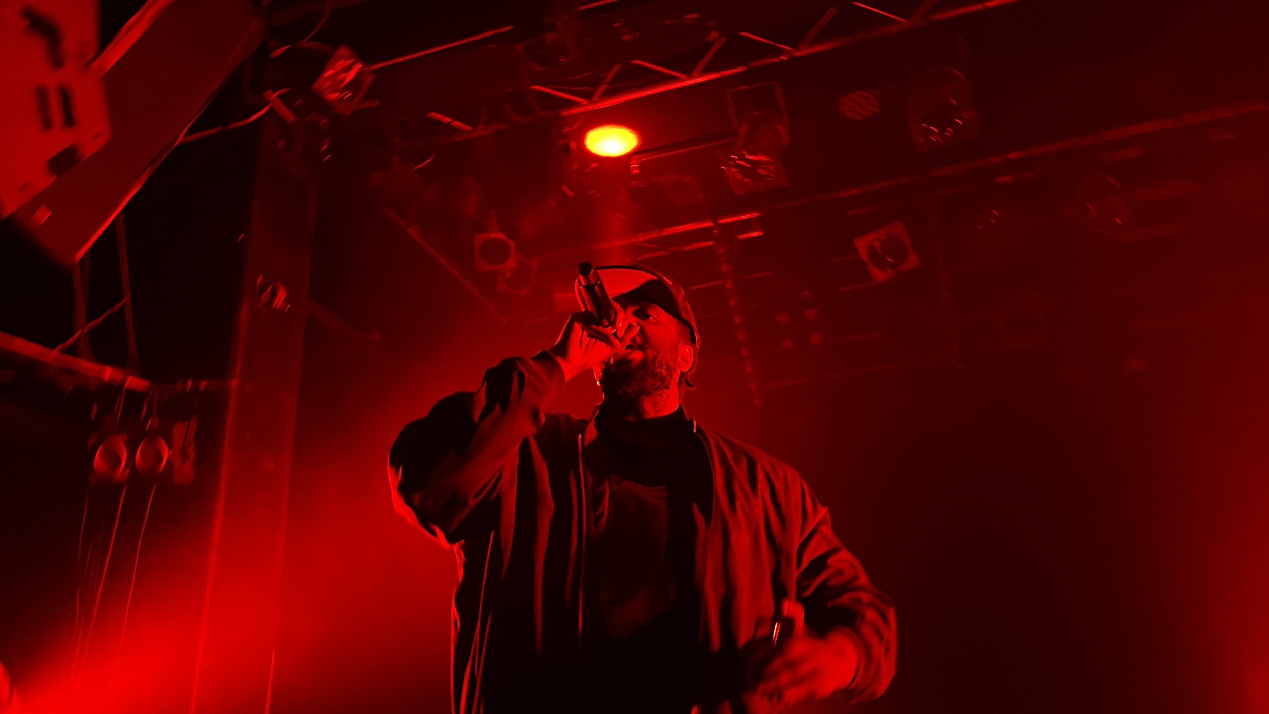 Un rappeur en concert, tenant un microphone, éclairé par des lumières rouges.