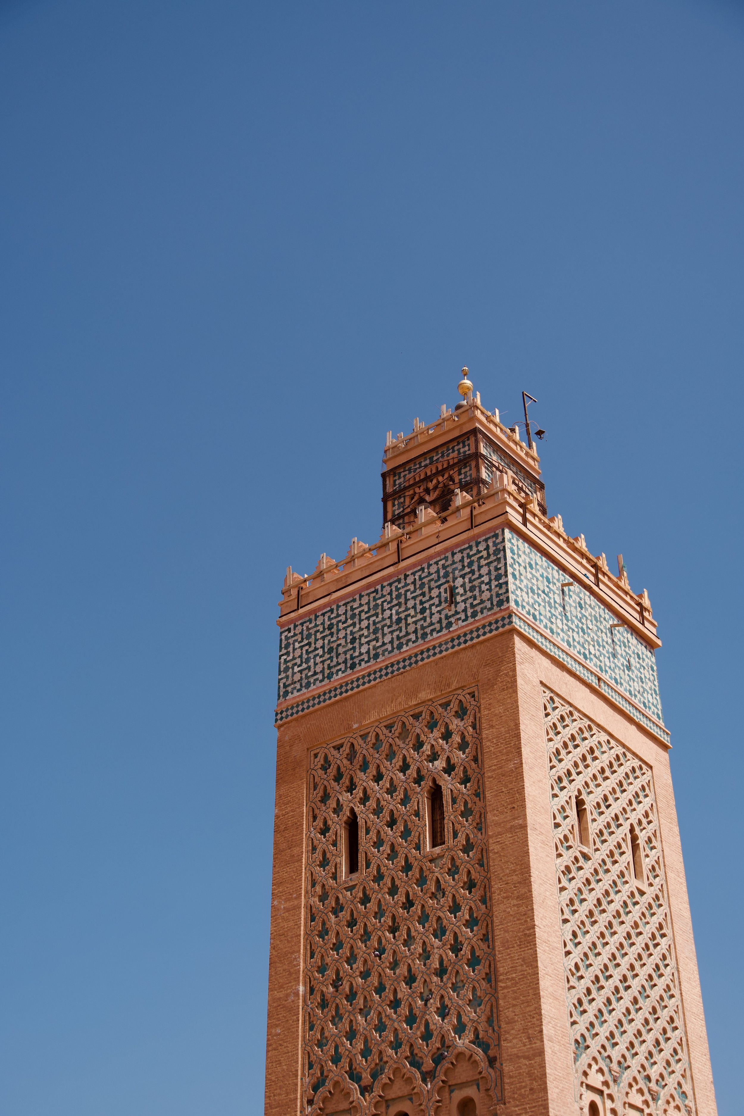 Minaret orné de motifs géométriques sous un ciel bleu clair.