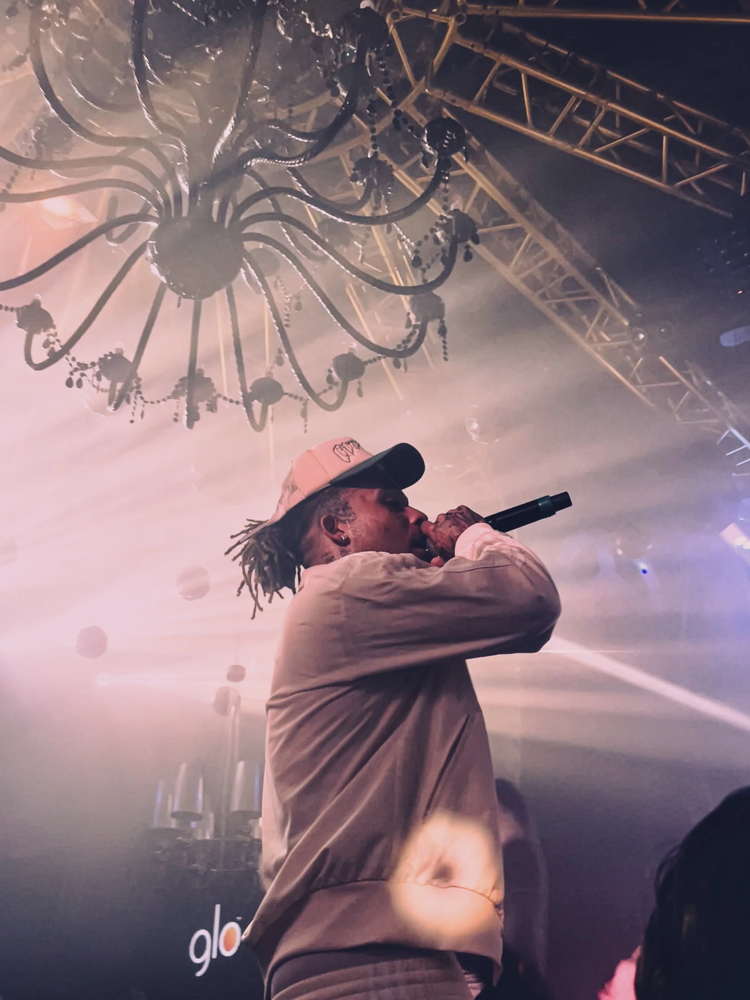 Artiste Zola chantant sur scène avec micro, éclairages de concert et lustre au plafond.