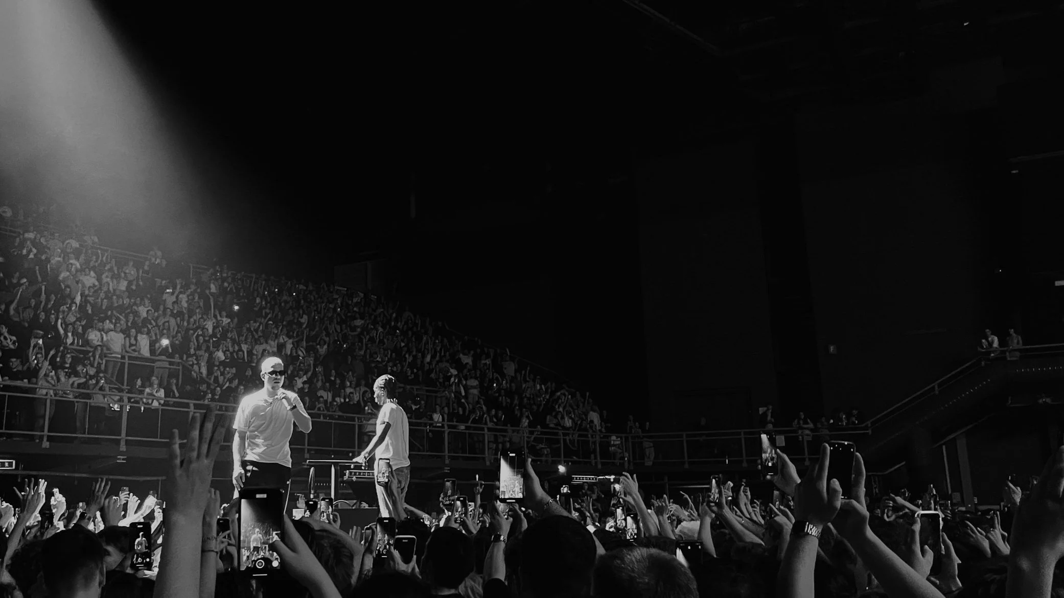 Concert PLK en noir et blanc avec deux artistes sur scène devant une foule enthousiaste.