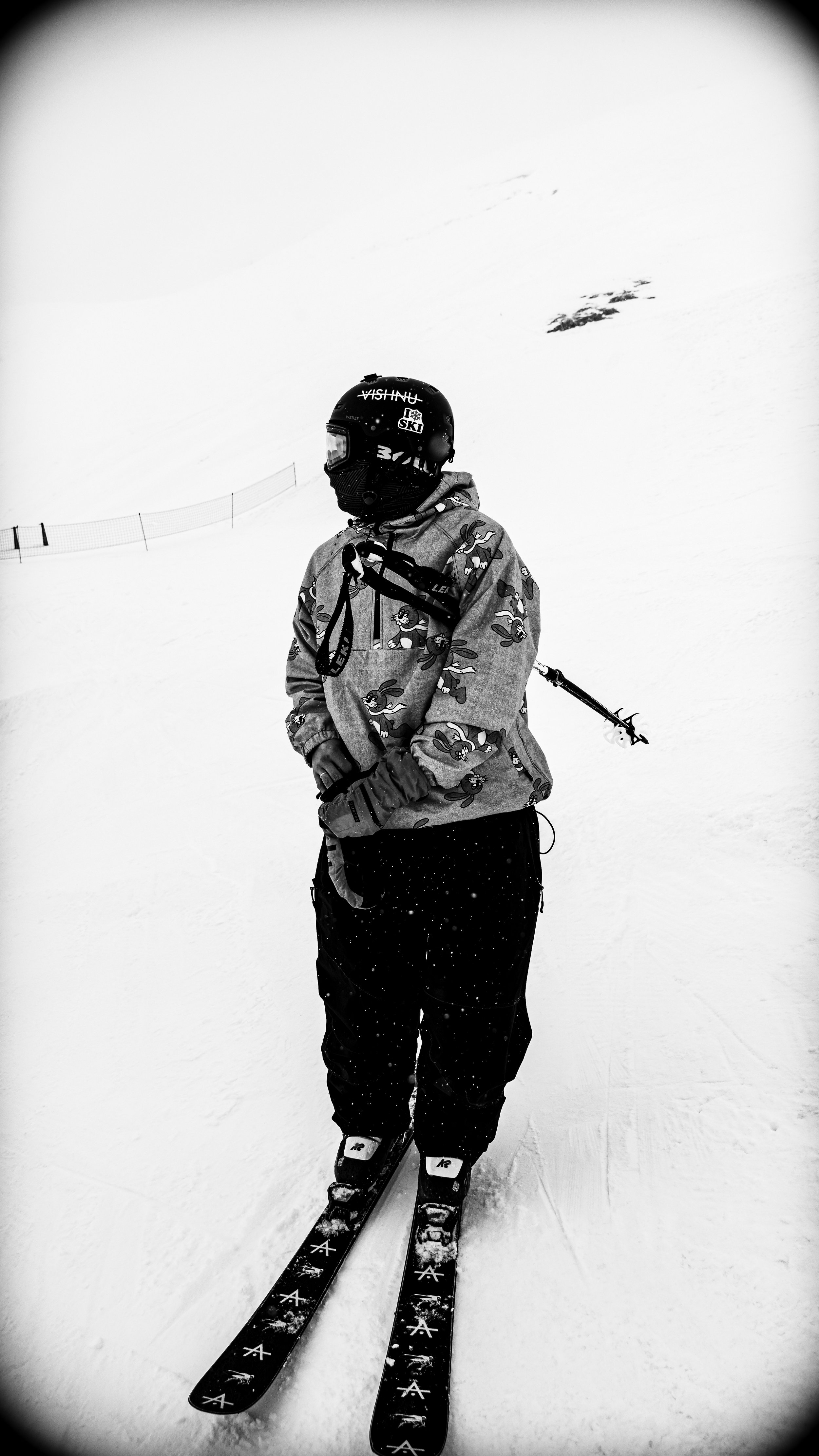 Une personne sur des skis freestyle en tenue de ski avec un casque et des lunettes, debout sur une pente enneigée.