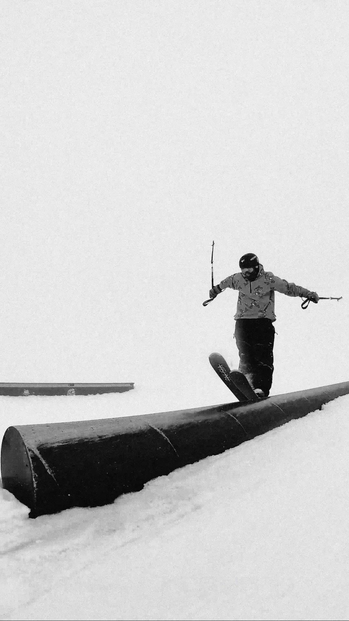 Skieur descendant une rampe enneigée, tenant des bâtons, en noir et blanc.