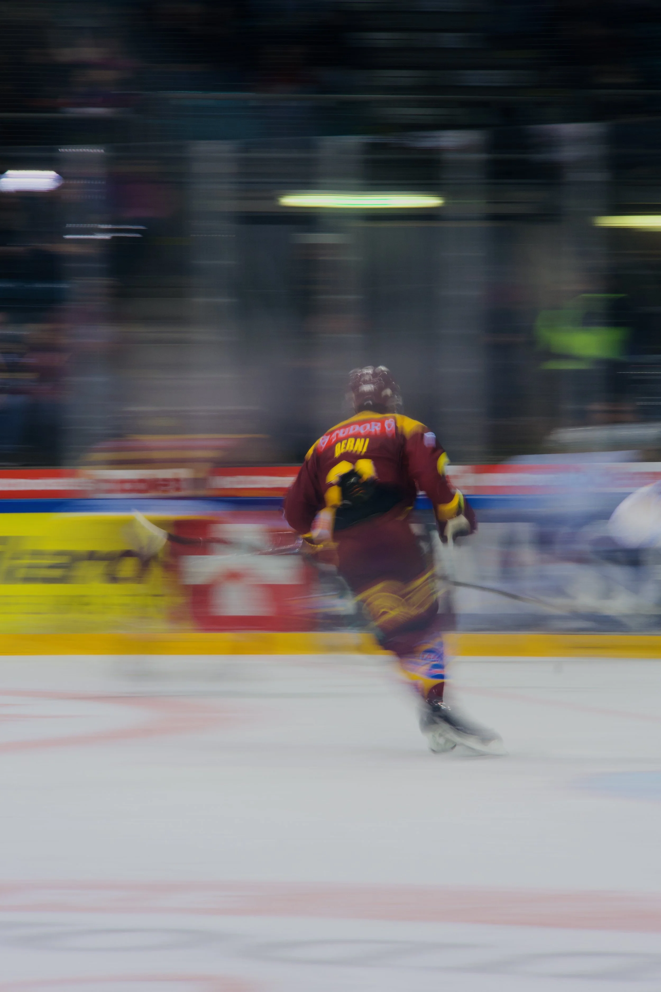 Un joueur de hockey sur glace en maillot bordeaux patine à grande vitesse sur la glace. L'arrière-plan est flou, indiquant le mouvement rapide.