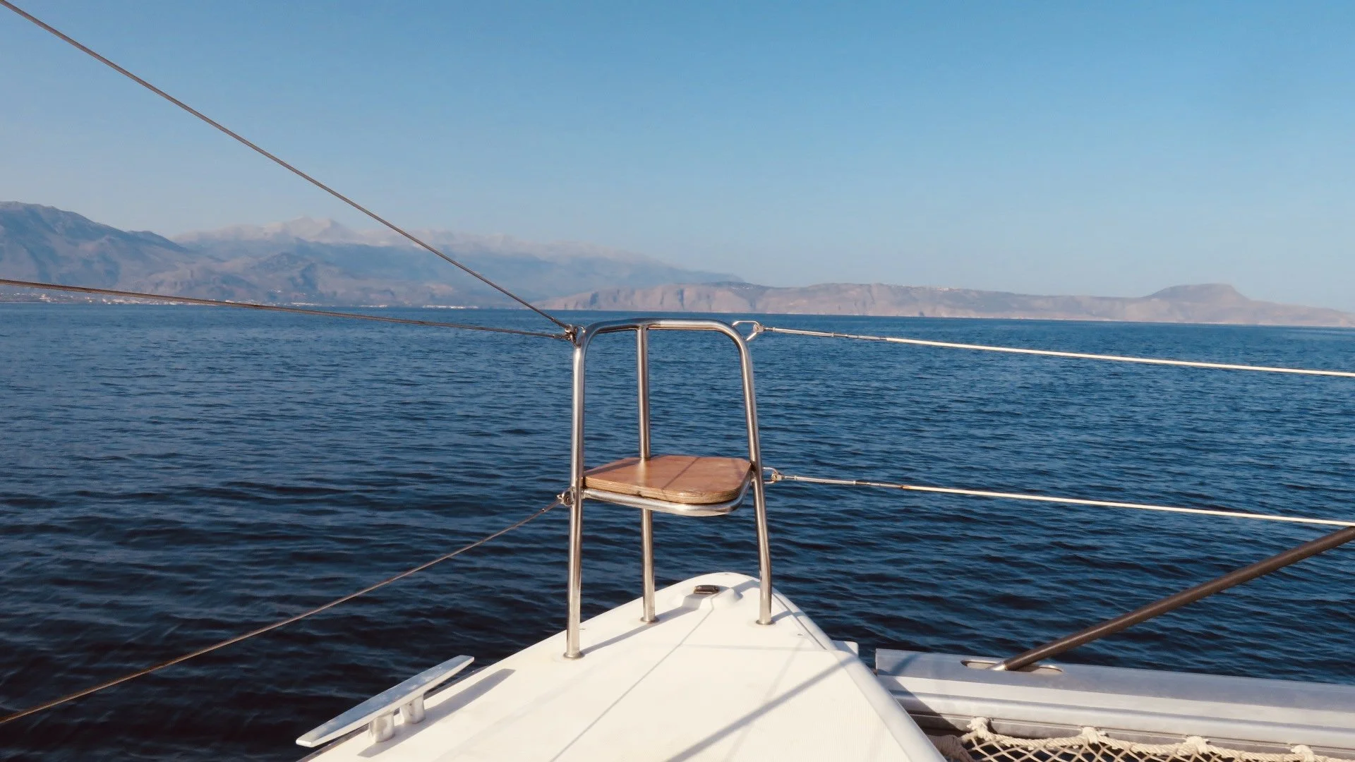 Bateau à voile sur la mer avec vue sur des montagnes lointaines sous un ciel bleu clair.