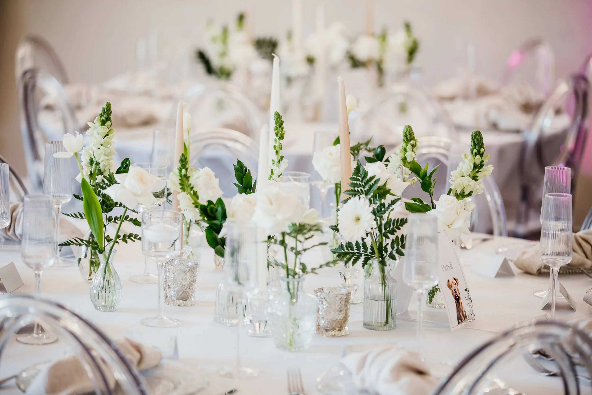 Elegant wedding reception table decorated with white flowers, candles, and glassware.