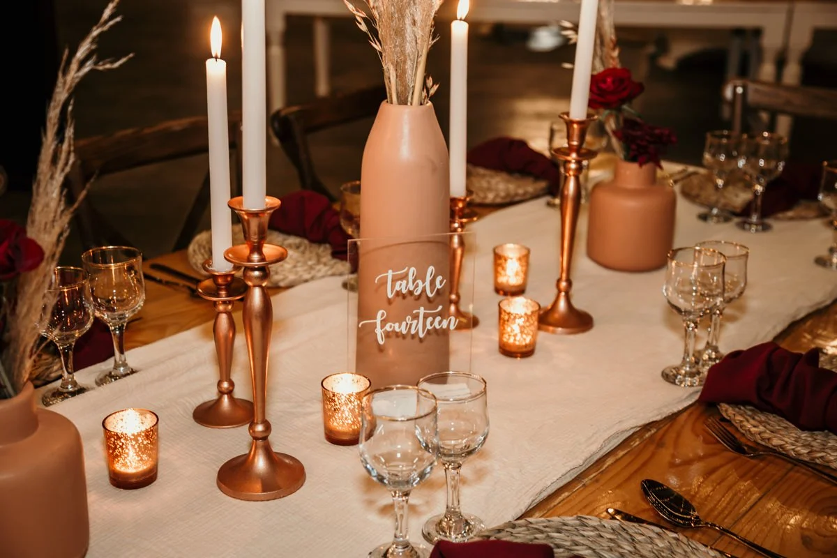 Elegant dinner table setting with candles, vases, wine glasses, and a table number sign that reads 'Table Fourteen'.