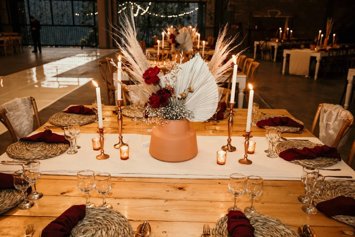 A decorated dining table with a floral centerpiece, candles, and place settings in a warmly lit event space.