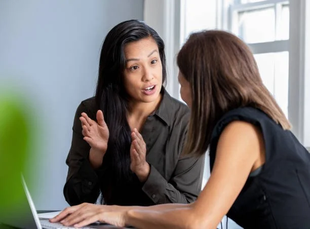 Two women having a discussion at a desk with a laptop