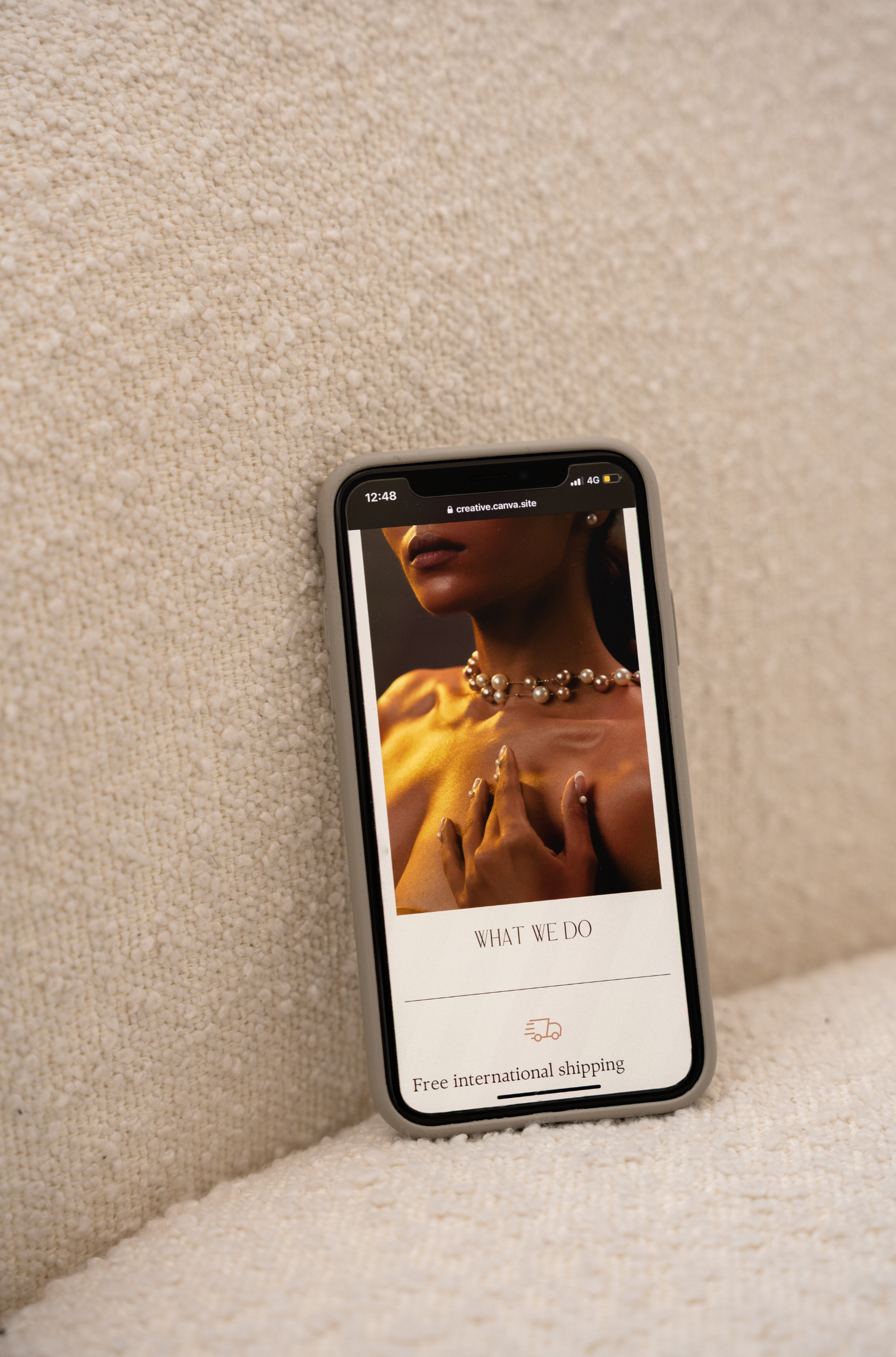 Smartphone displaying fashion website with model wearing jewelry, on textured fabric surface.
