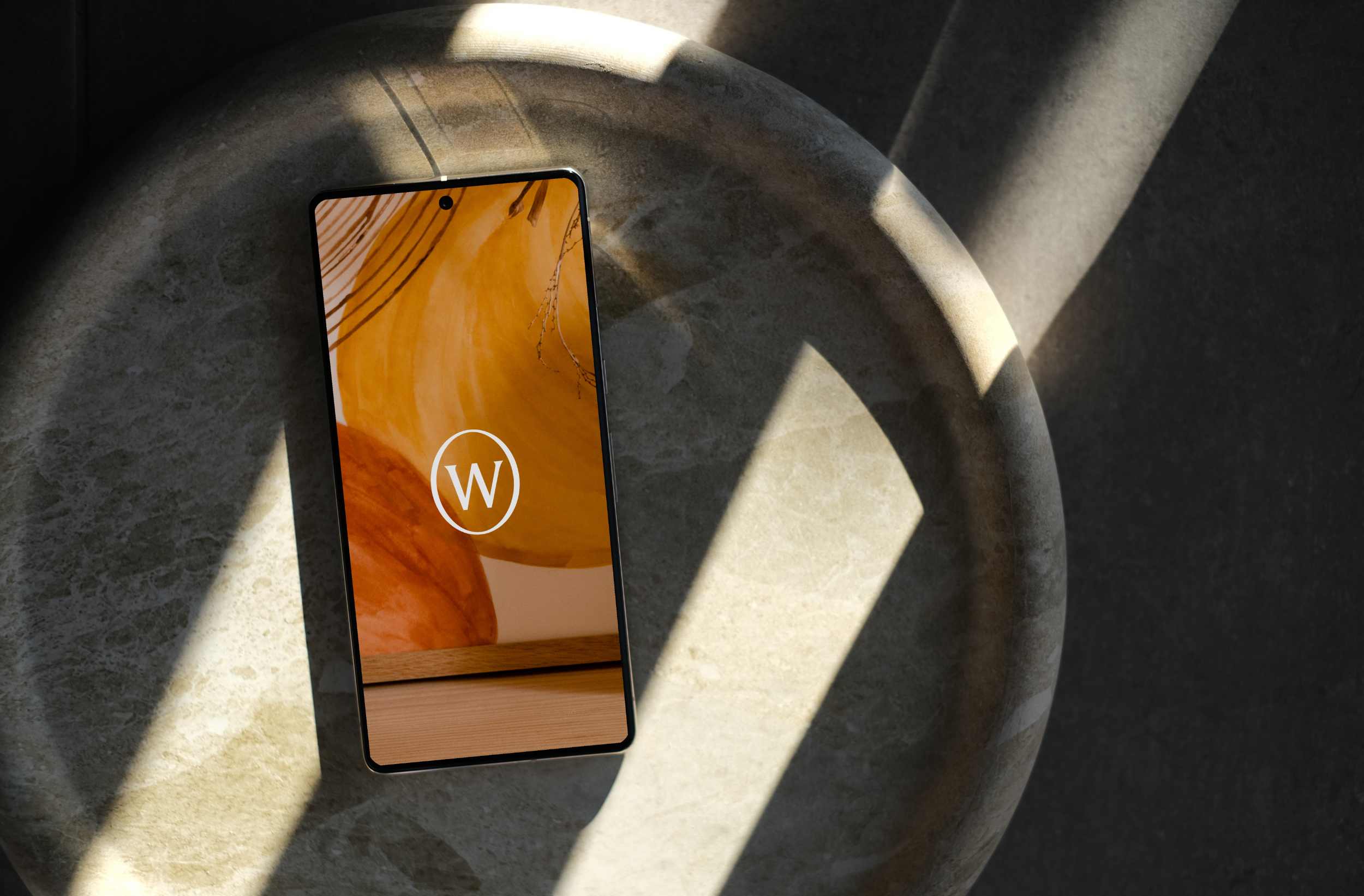 Smartphone with abstract background and "W" logo on circular surface in sunlight.
