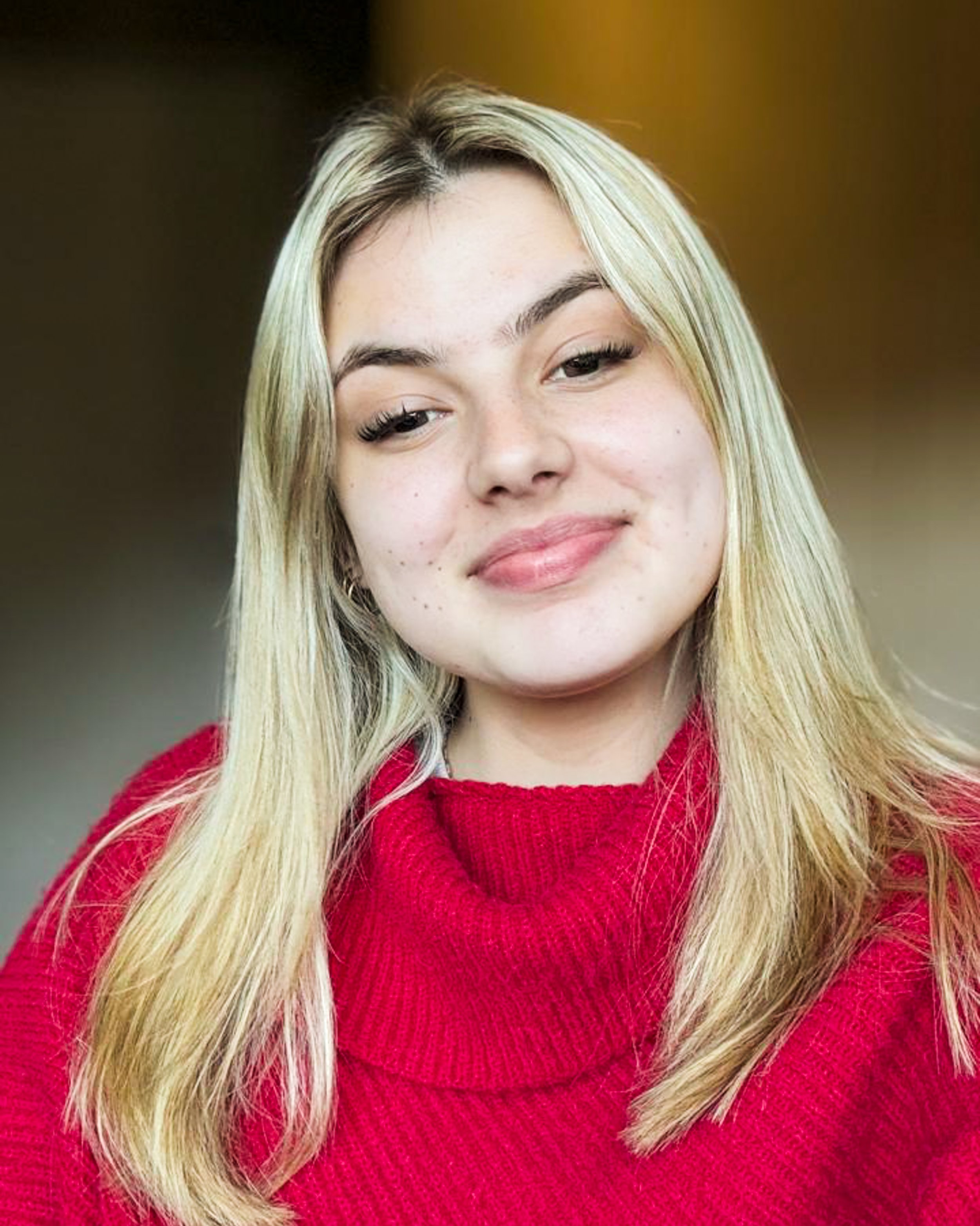 Hayley Stemmet, head of marketing at Supragas. Close-up of a young woman with long blonde hair, wearing a red sweater, smiling softly, with a blurred background.