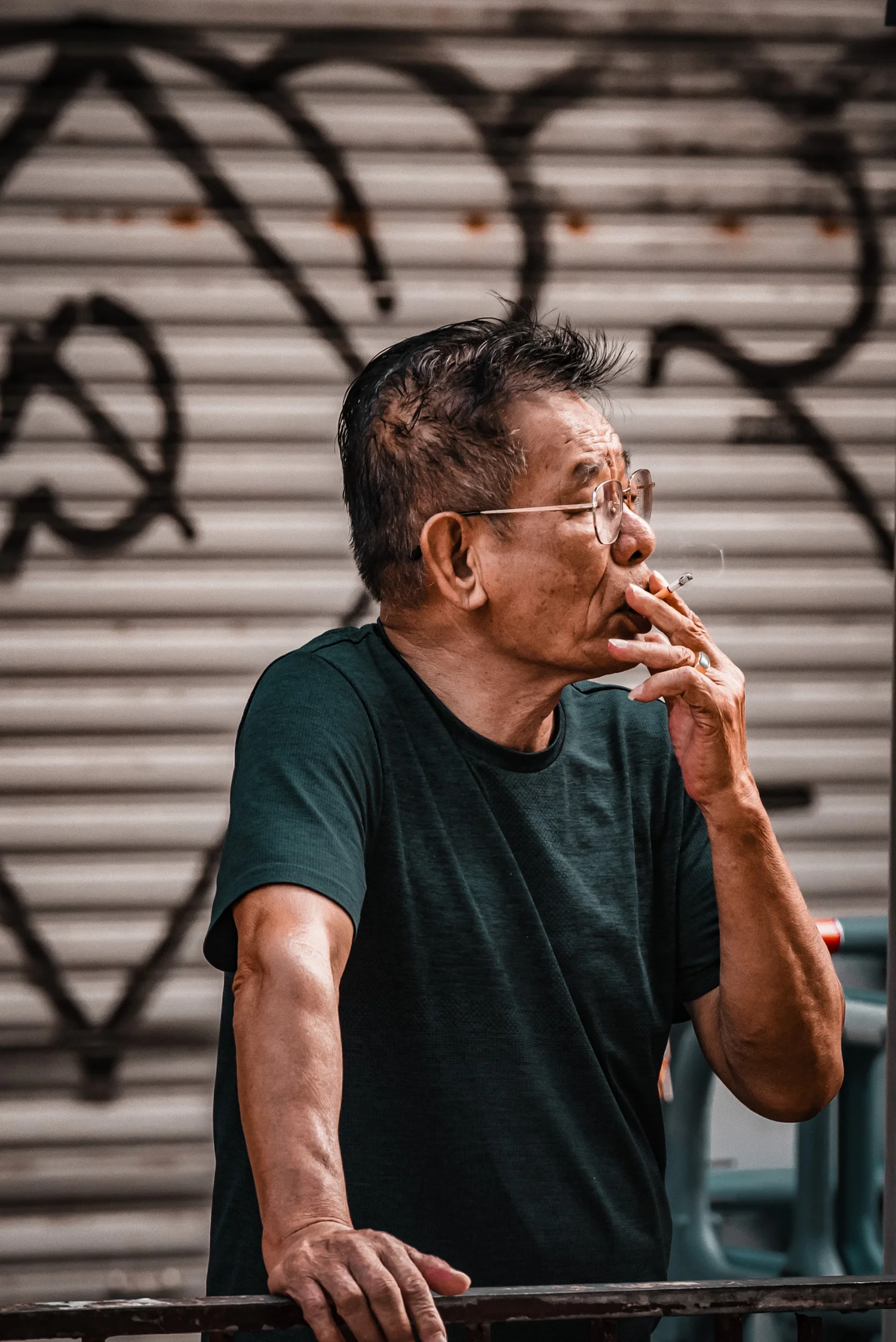 Street photograph of an older man smoking in front of a graffiti-covered shutter, Hong Kong