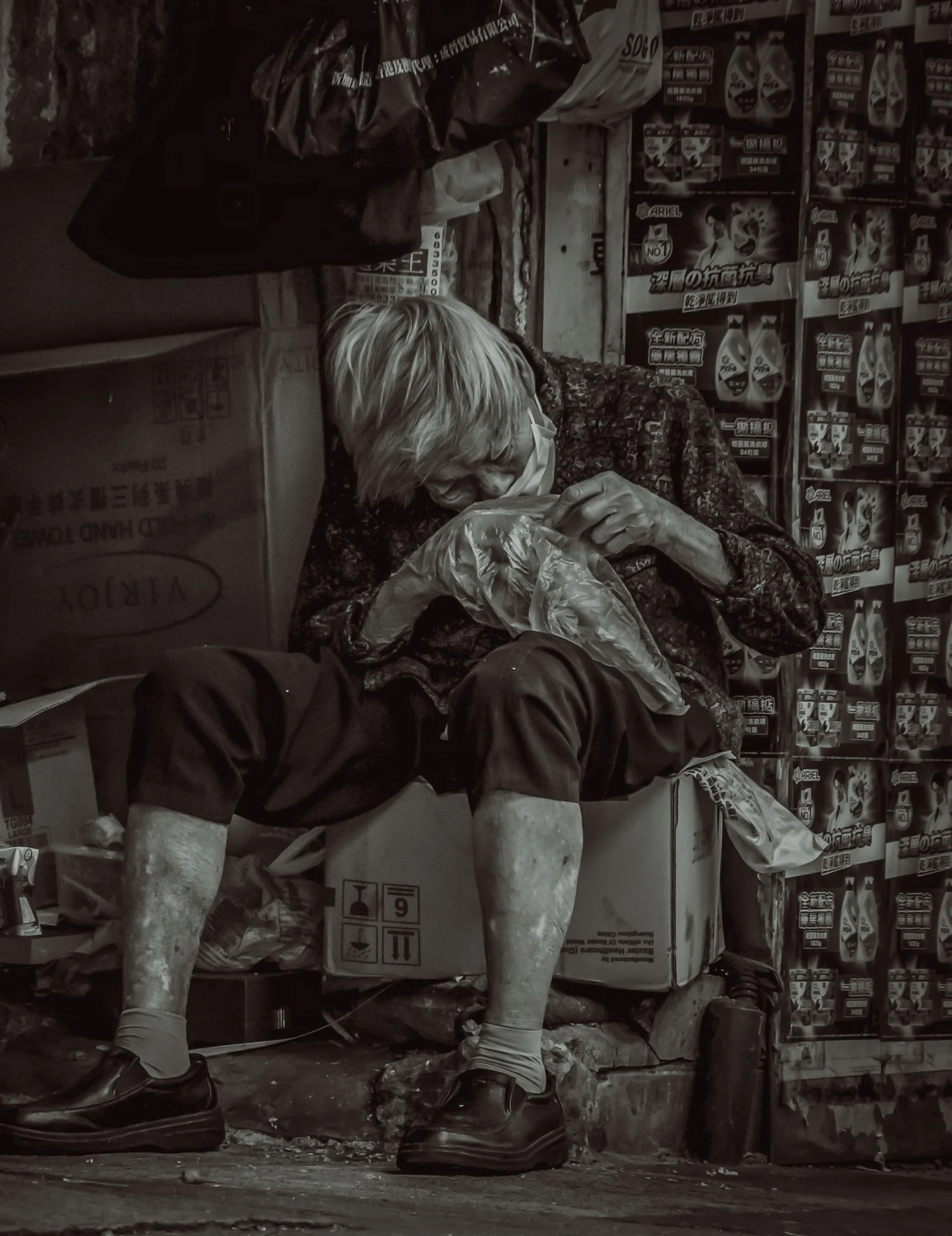 Elderly man resting on a stool beside a newsstand on a Hong Kong street