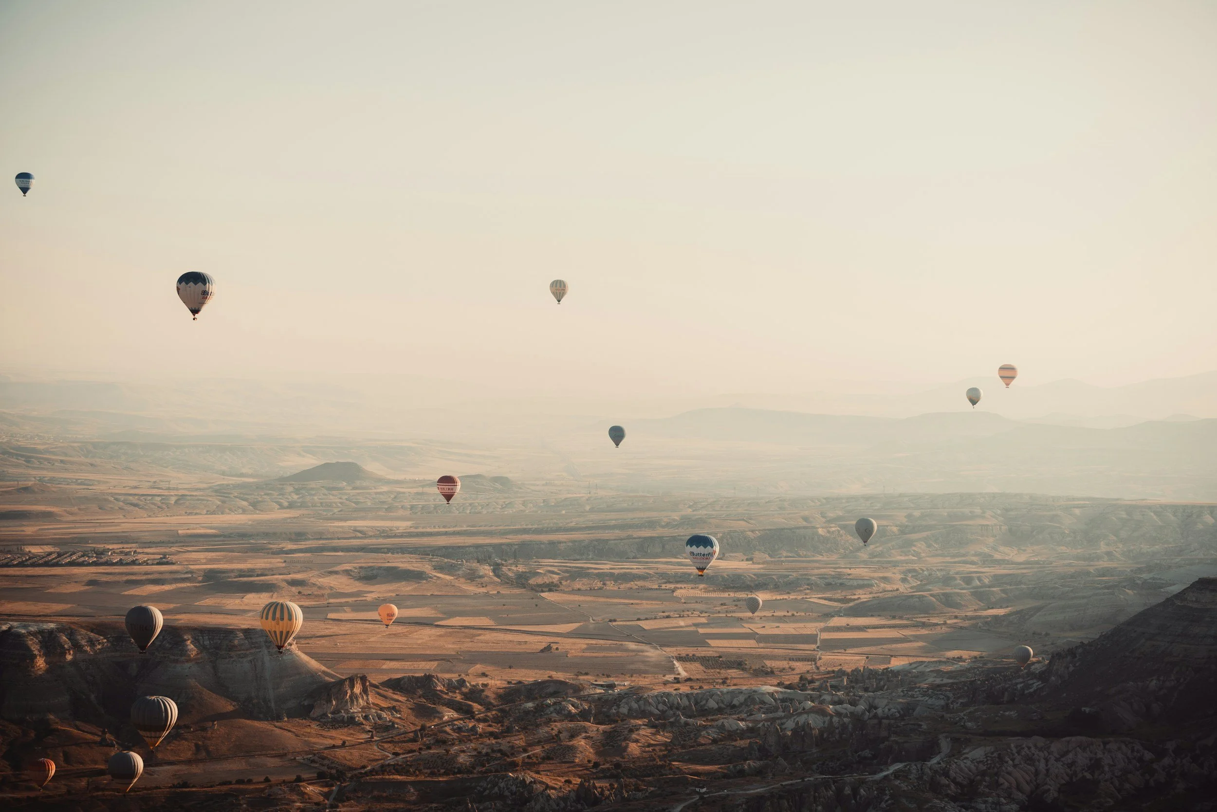 Uwe Steinhart, Steinhart Business, Heißluftballons über einer weiten, hügeligen Landschaft bei Sonnenaufgang.