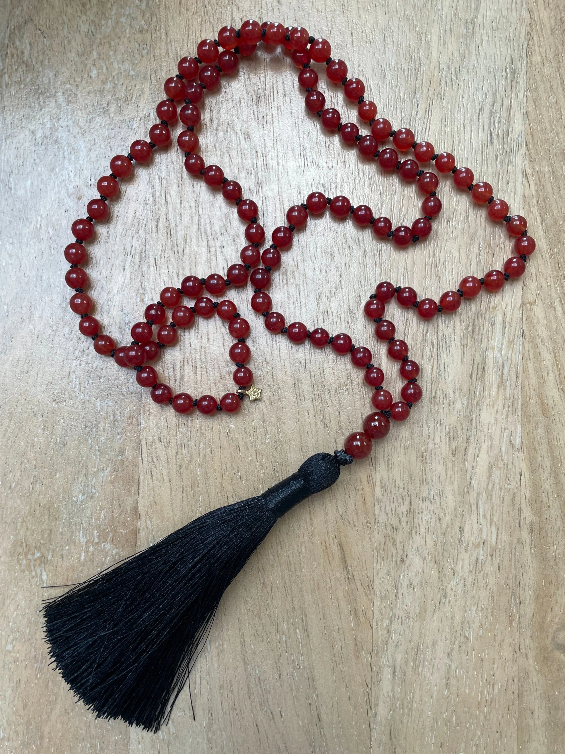 A Carnelian necklace with a black tassel and small gold star charm, arranged on a wooden surface.
